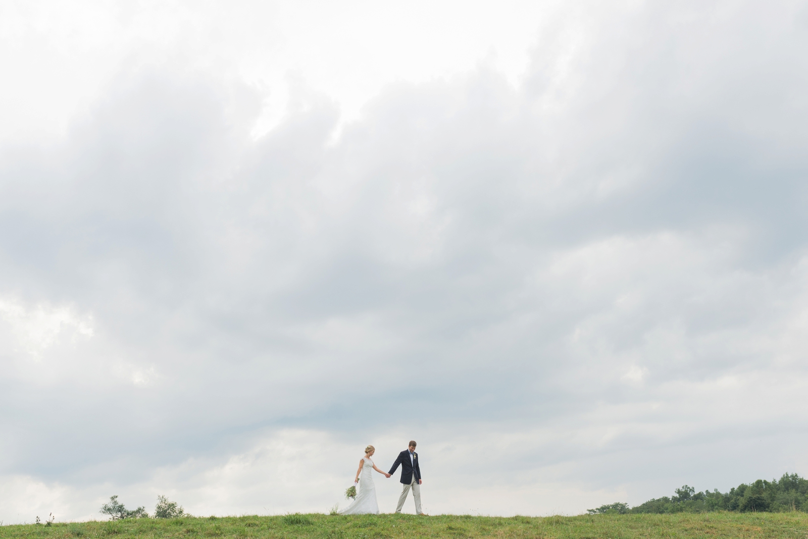 couple-walking-across-the-top-of-a-big-hill-with-dark-clouds-above-them