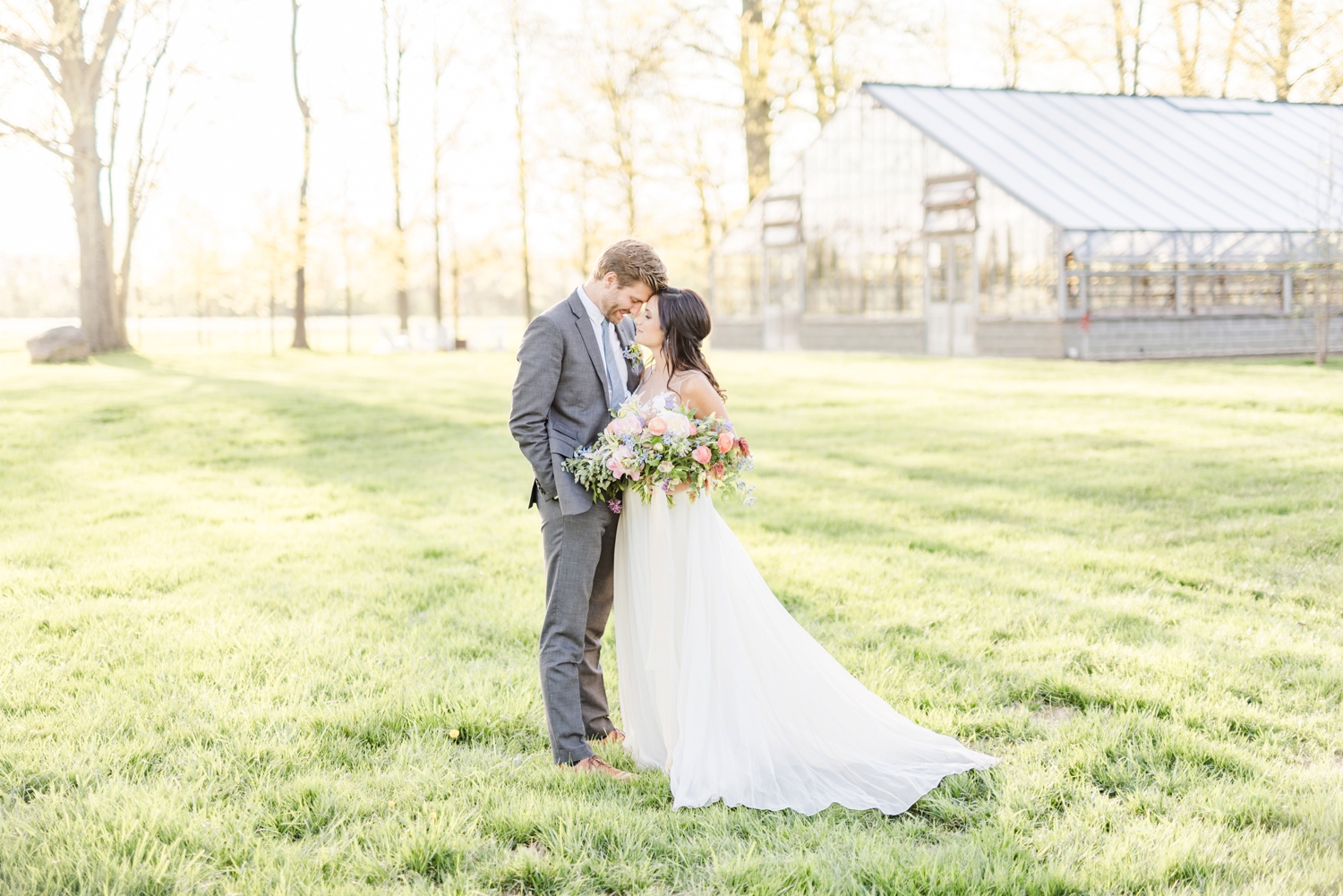 bride-and-groom-posing-in-a-field-in-front-of-a-beautiful-greenhouse-wedding-venue