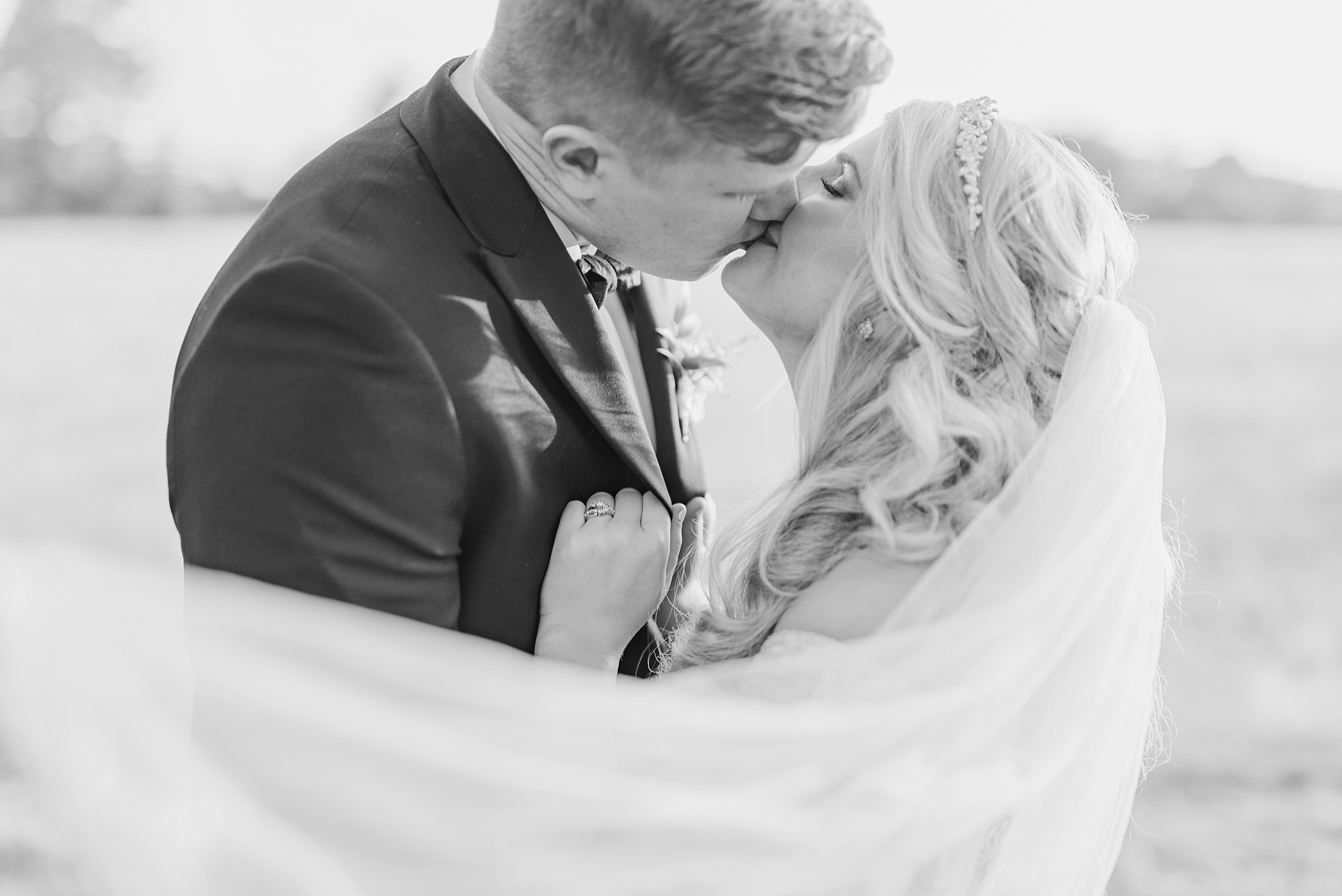 bride and groom kiss during wedding portraits while veil wraps around them