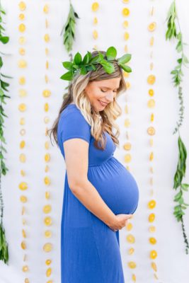 mom wearing green floral crown holds belly photographed in front of citrus backdrop