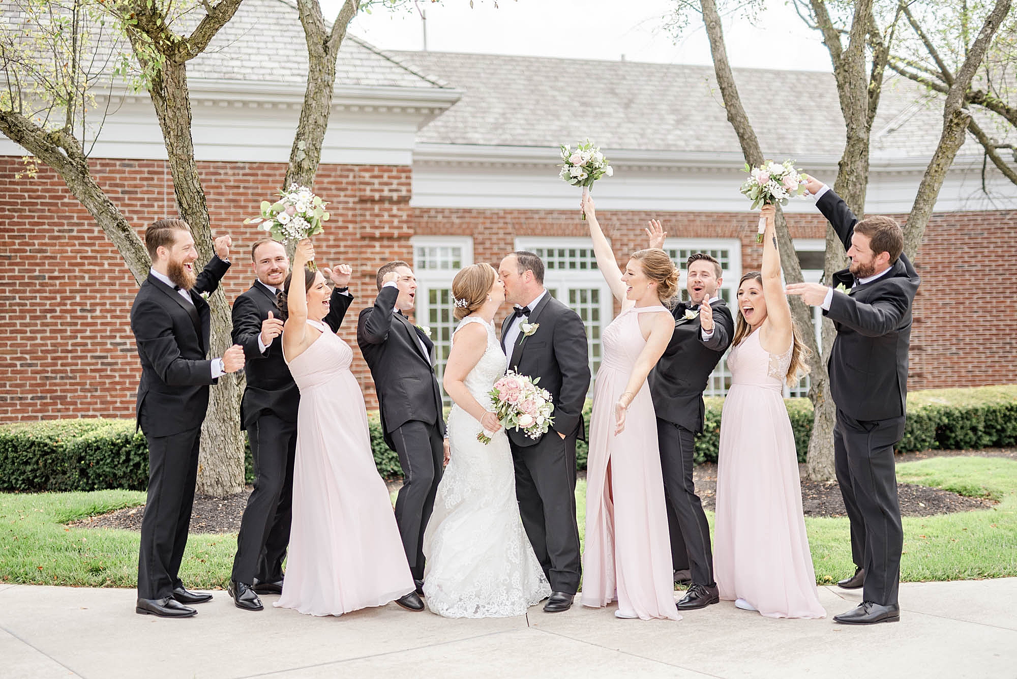 bridesmaids and groomsmen cheer while bride and groom kiss