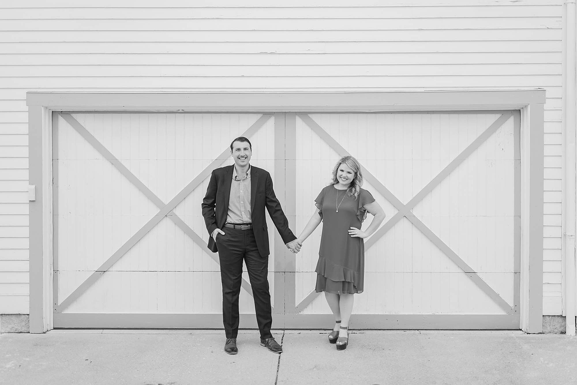 engaged couple holds hands posing by barn door