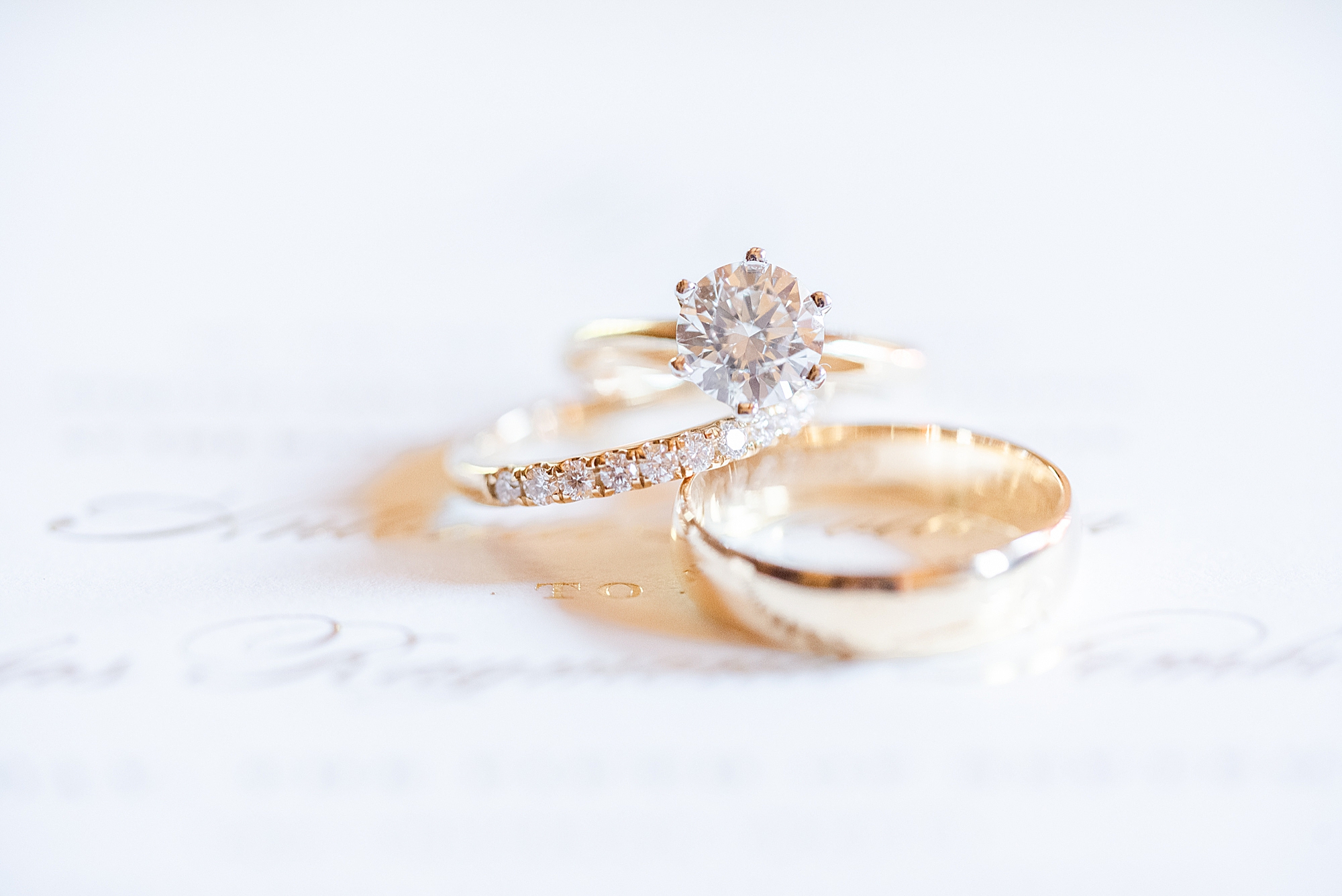 gold wedding rings lay on wedding invitation
