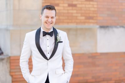 groom in white tux poses outside church in Ohio