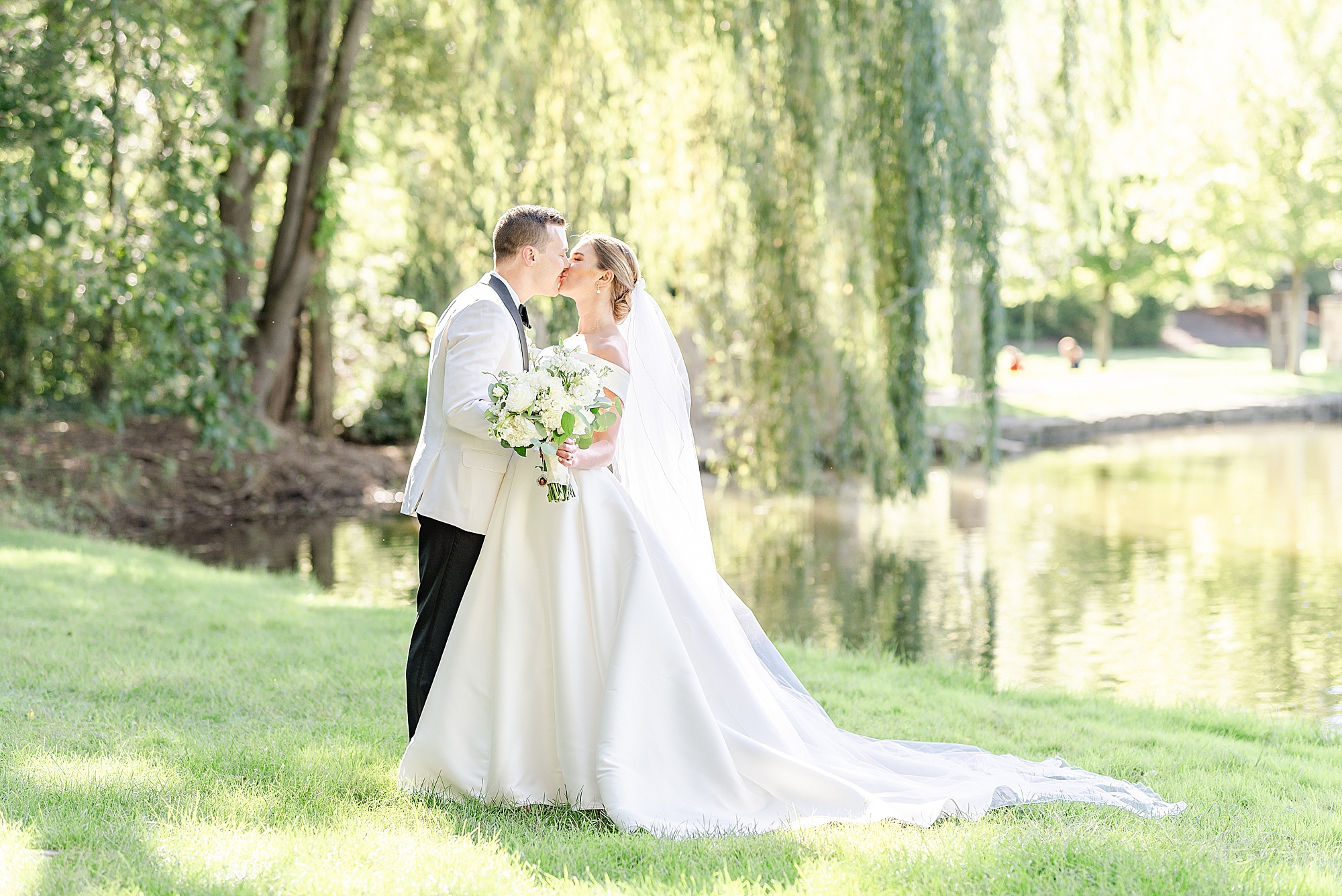 newlyweds kiss under weeping willow at Gervasi Vineyard