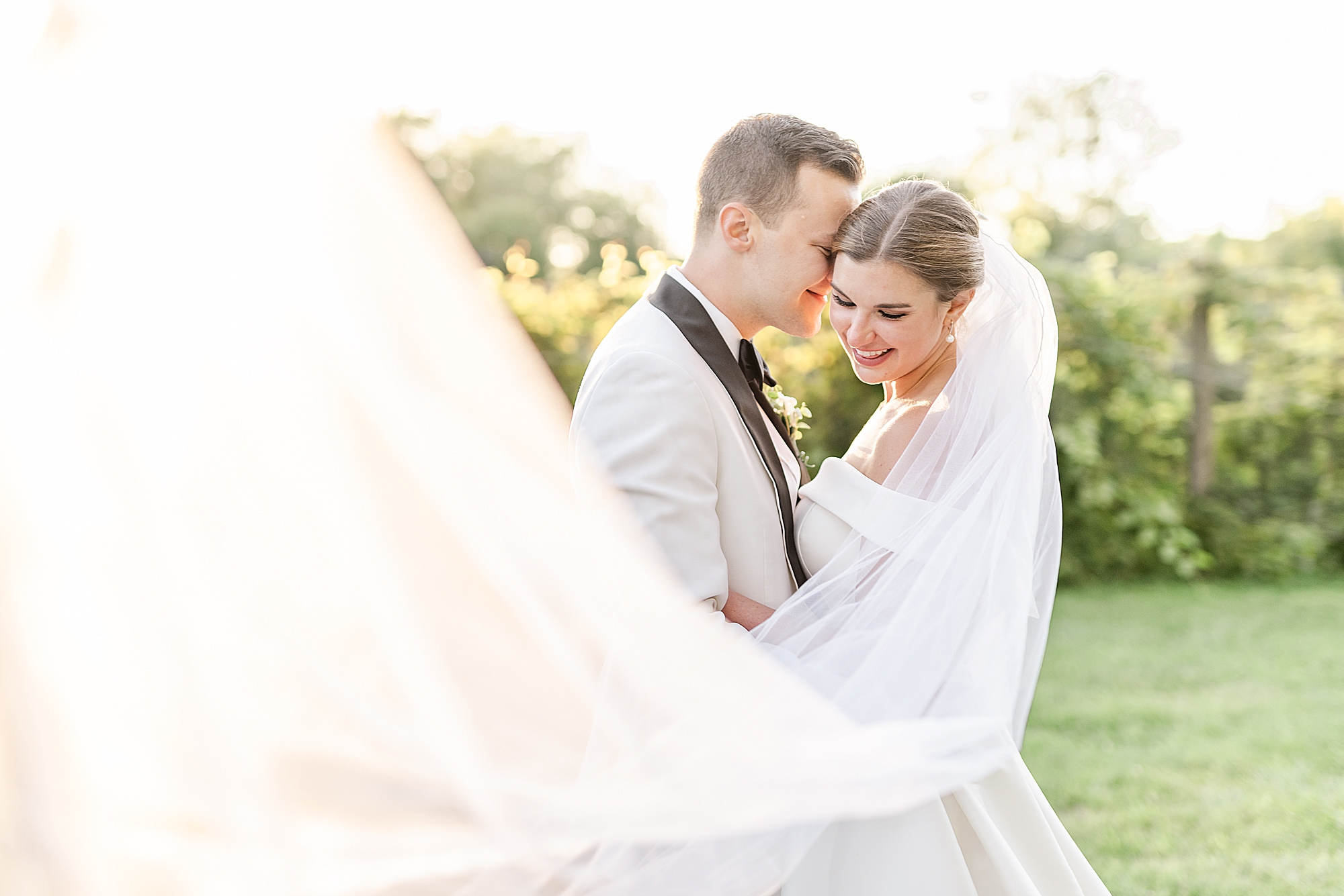 bride and groom smile while veil twists in the wind