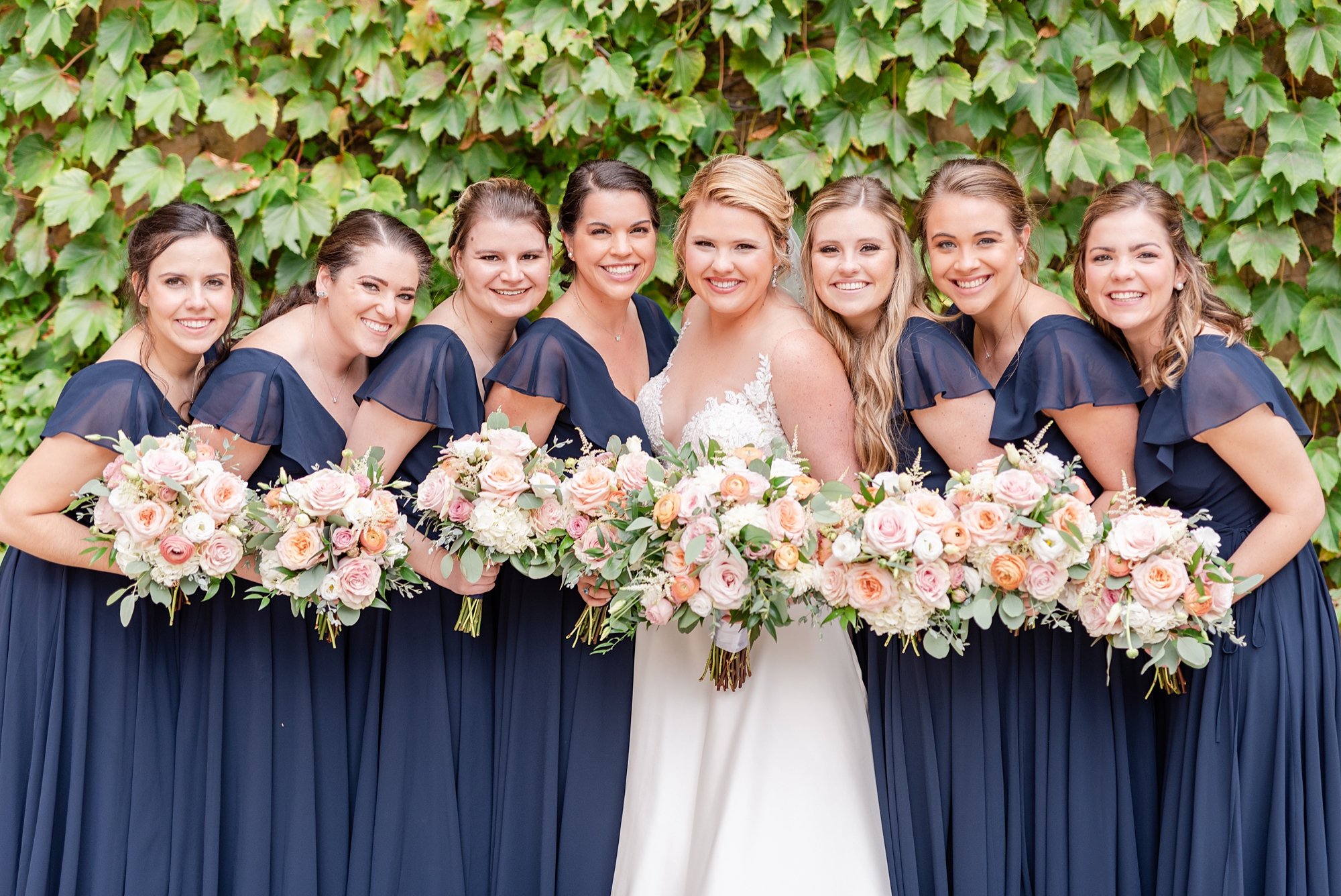 bridesmaids in navy gowns pose outside ivy wall at The Club at Corazon