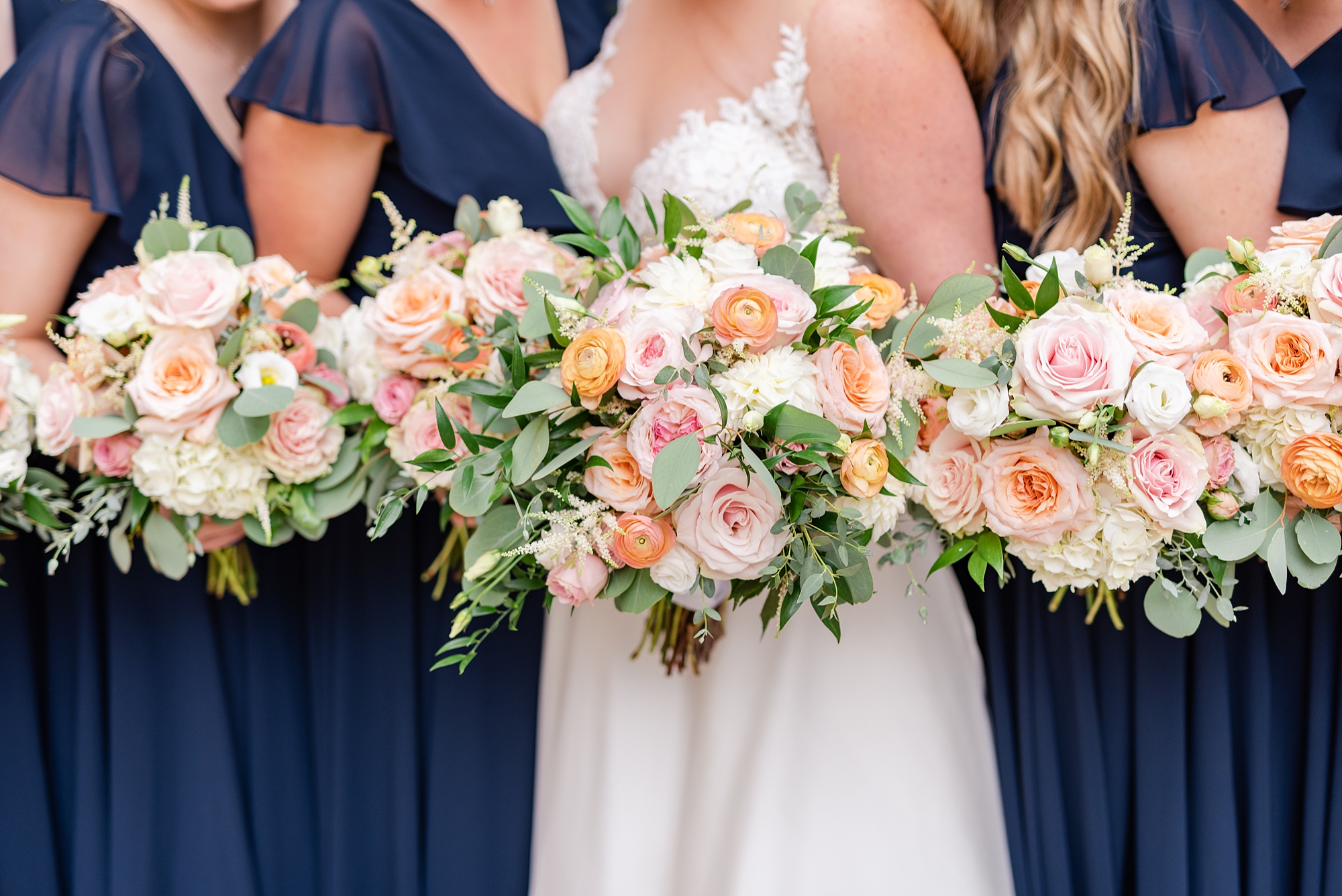 bridesmaids in navy dresses hold bouquets with pink flowers