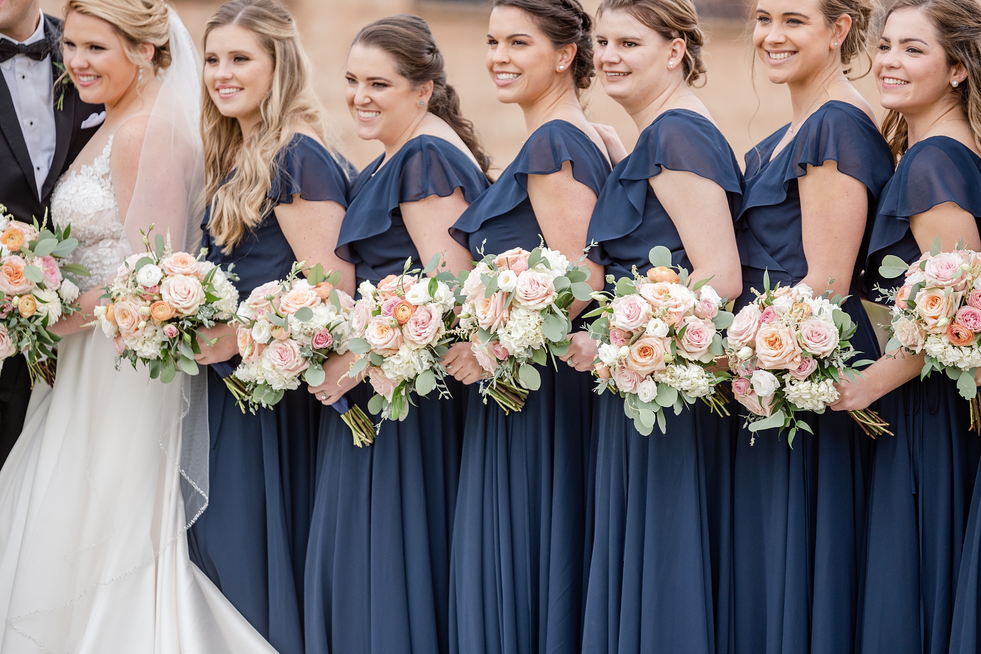 bridesmaids in navy gowns hold bouquets with ivory and pink flowers