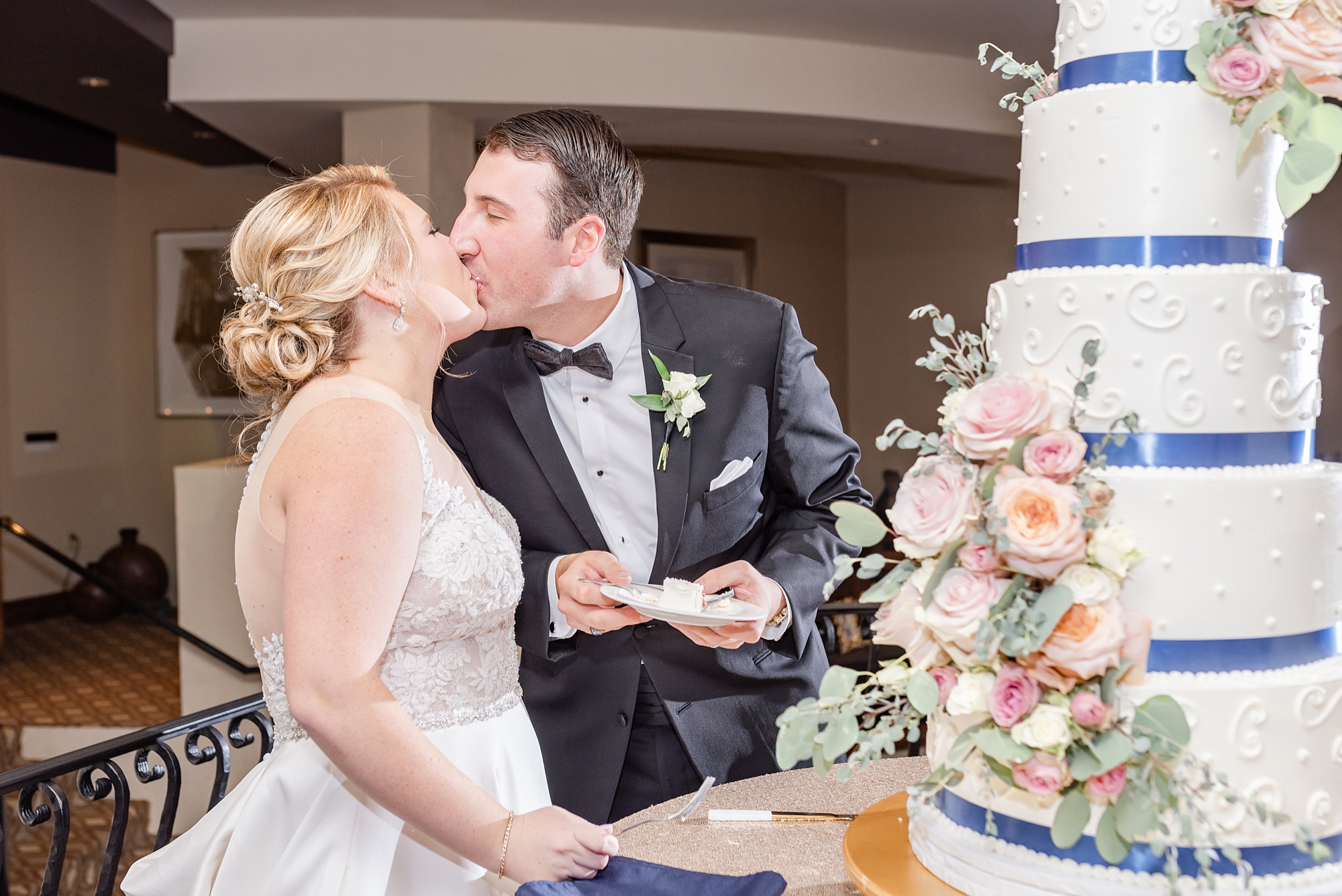 bride and groom kiss while cutting wedding cake