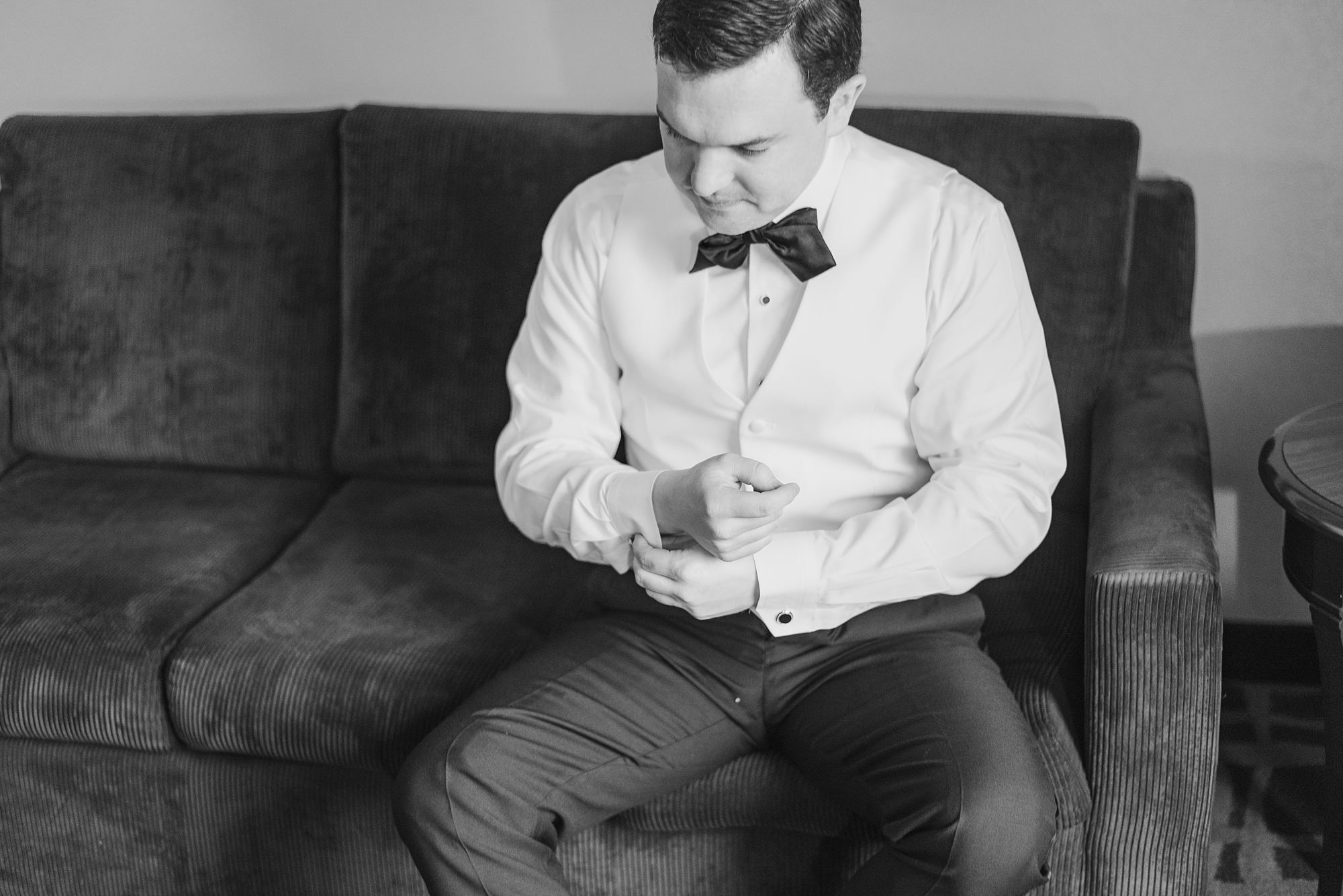 groom sits on couch and adjusts cufflinks
