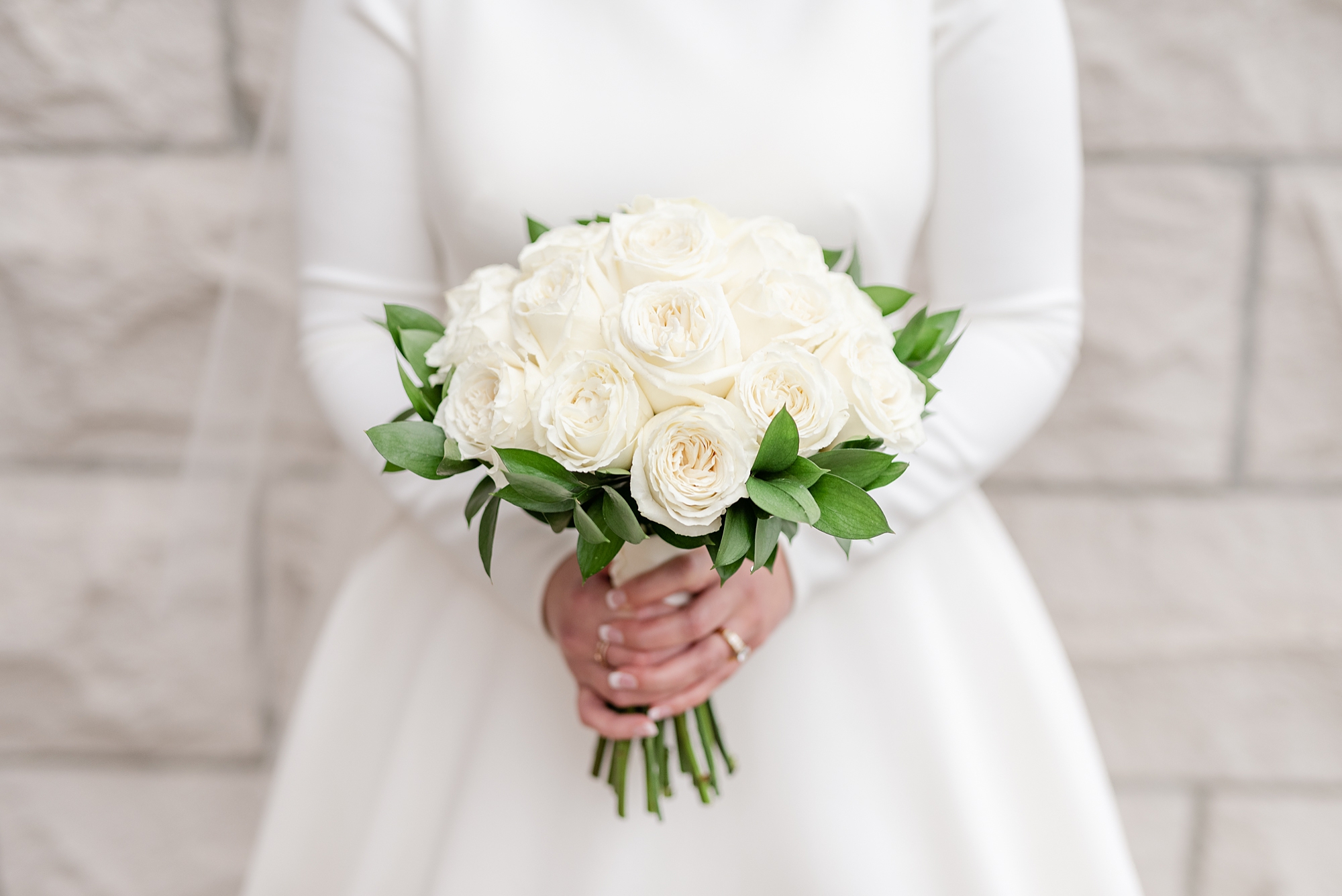 bride holds all white bouquet of roses