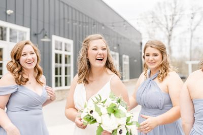 bride laughs during spring wedding photos with bridesmaids in blue gowns