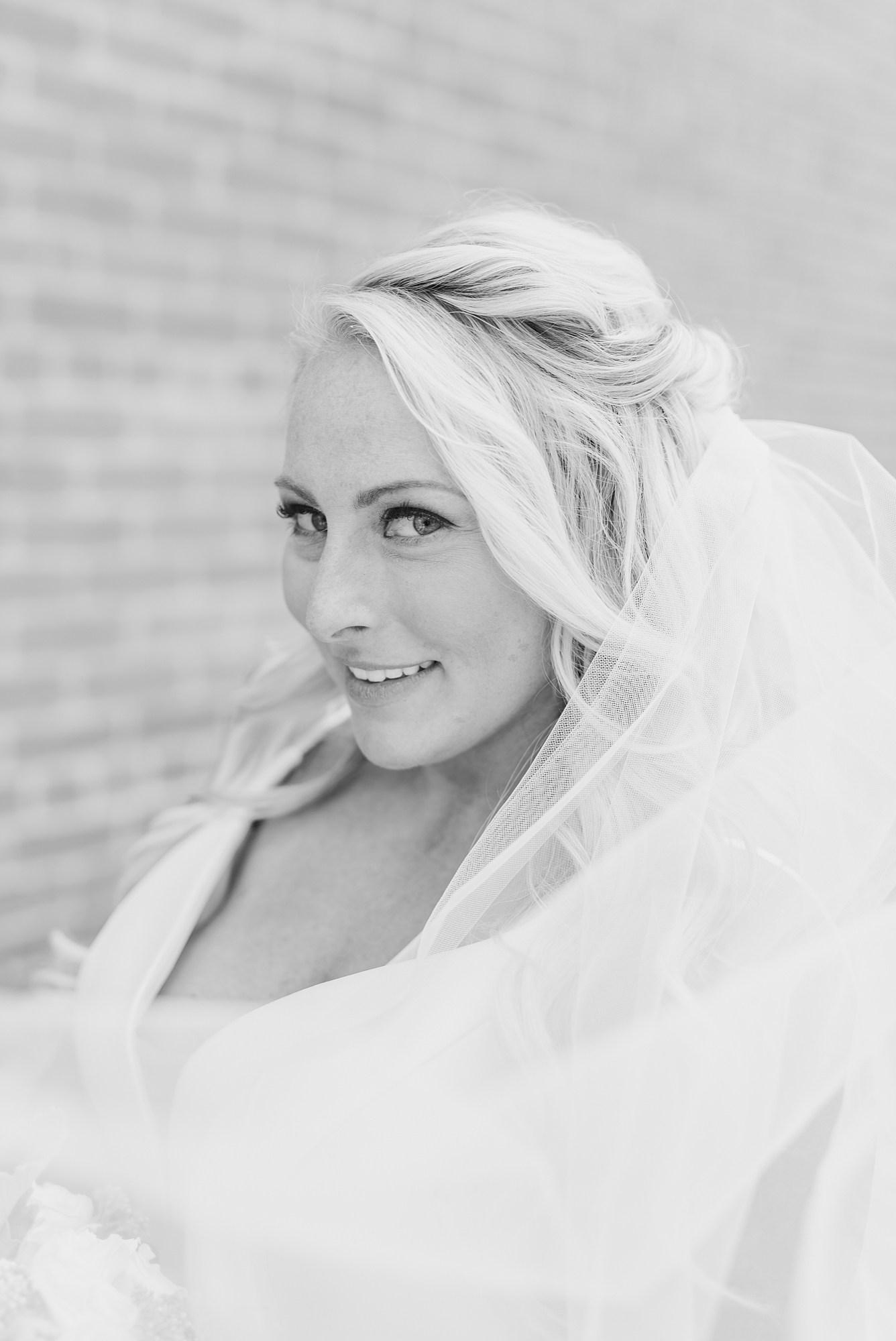 bride smiles at photographer with veil around shoulders