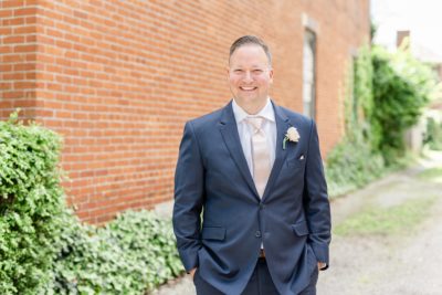 groom poses in navy suit with pink tie