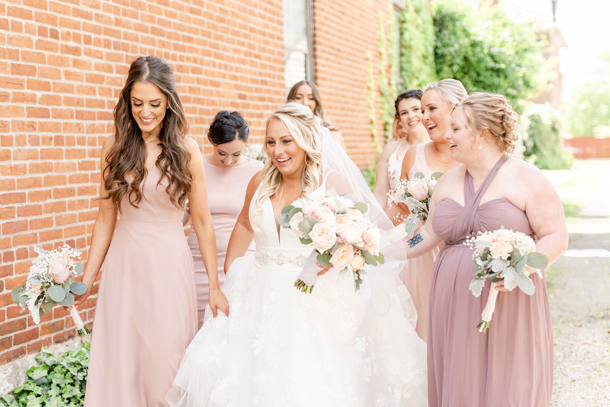 bride walks with bridesmaids in mismatched pink gowns