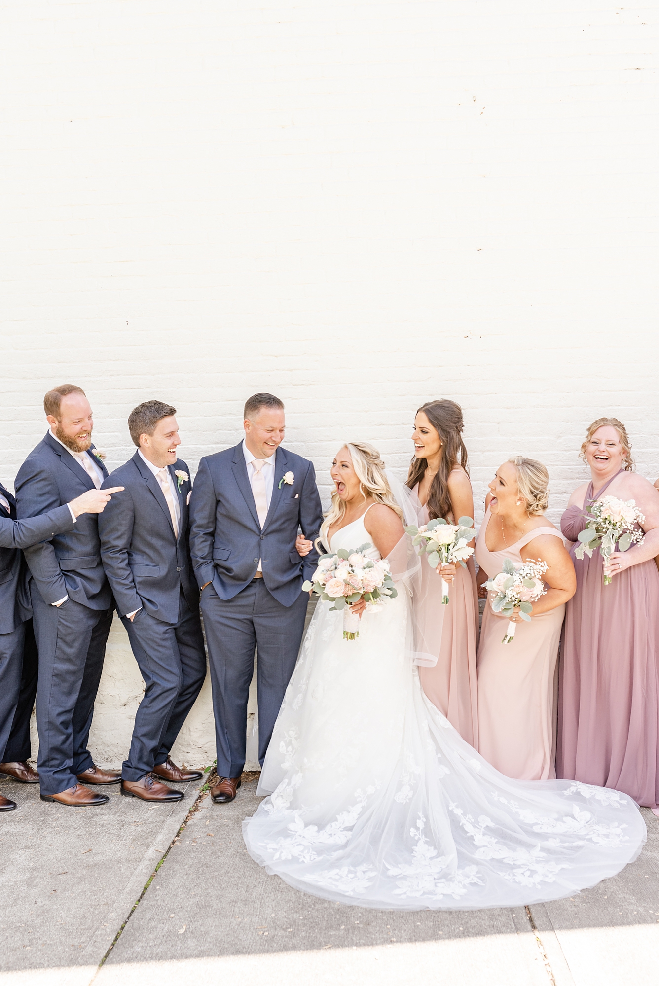 bride and groom laugh with bridal party by white wall in Columbus OH
