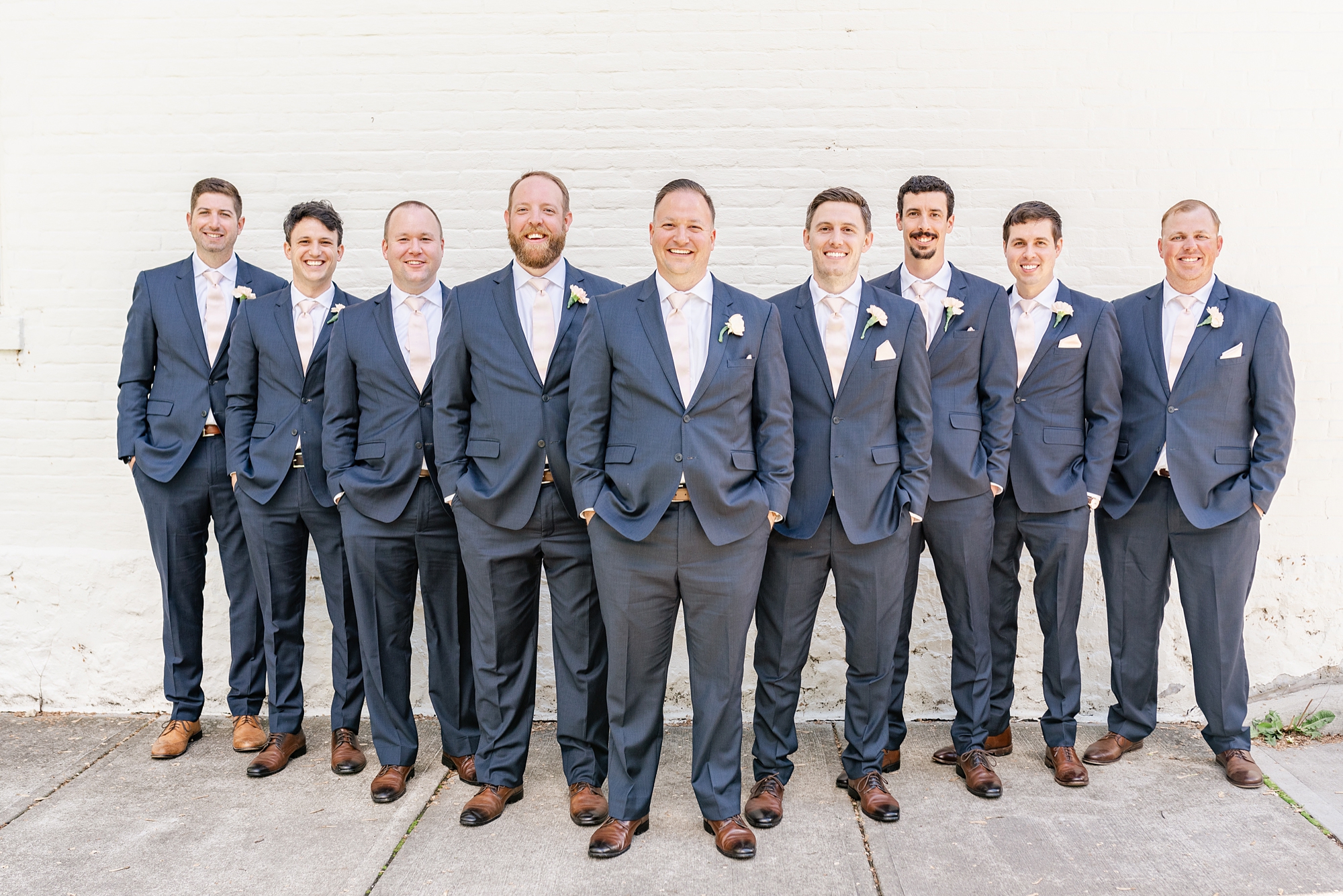 groom and groomsmen in navy suits pose by white wall in Ohio