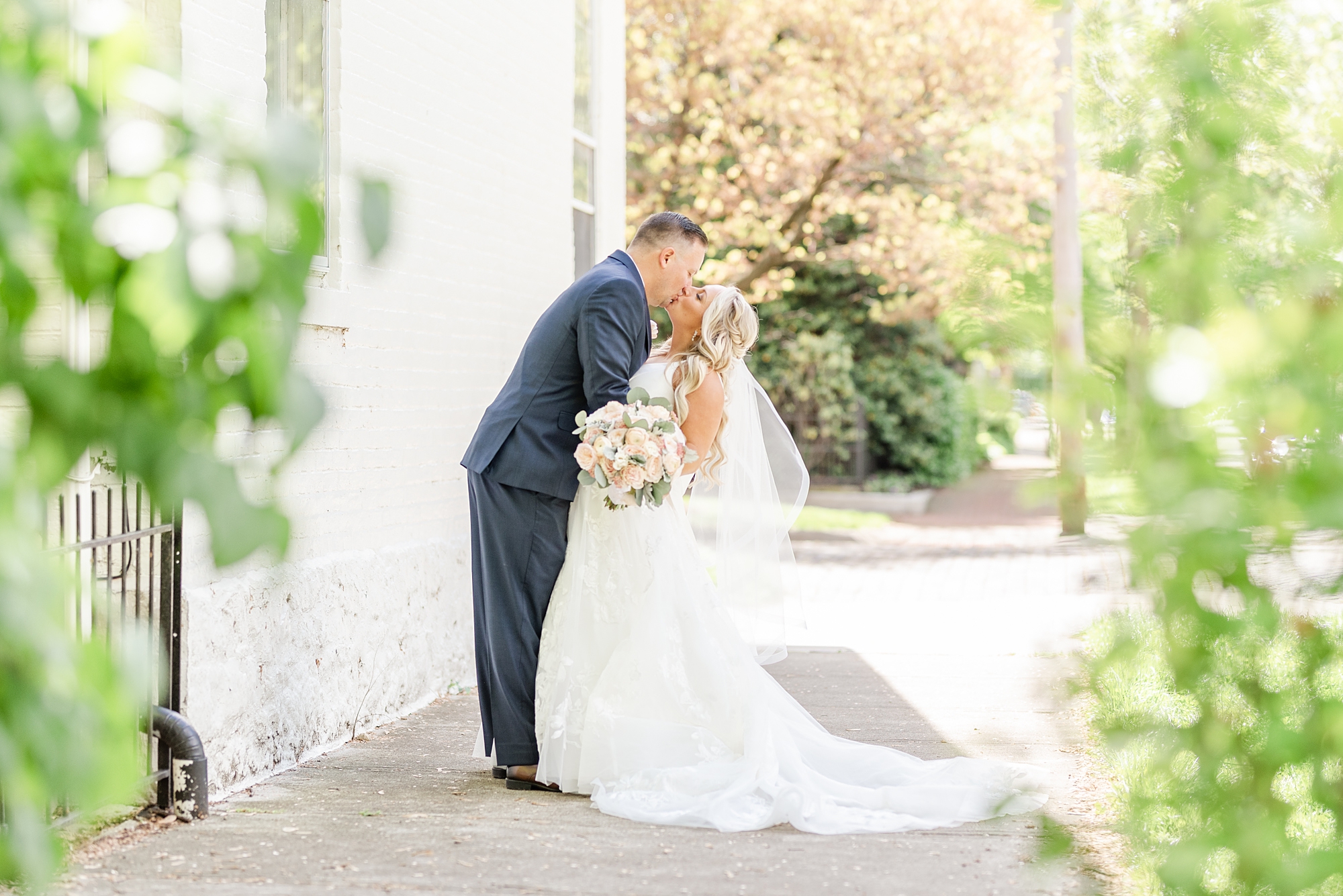bride and groom kiss by white wall in Ohio