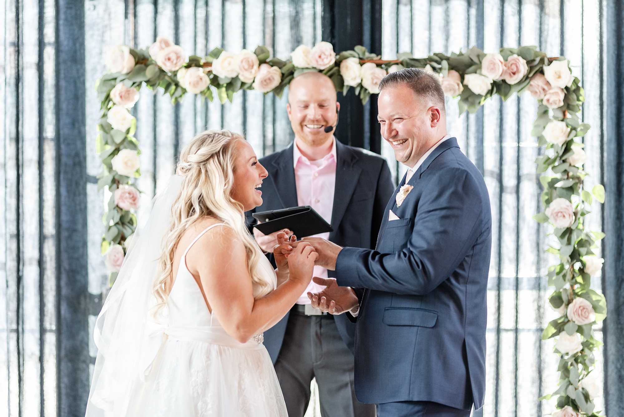 newlyweds laugh together during High Line Car House wedding ceremony by floral arch