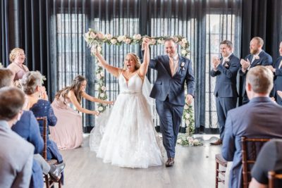 newlyweds cheer after High Line Car House wedding ceremony by floral arch