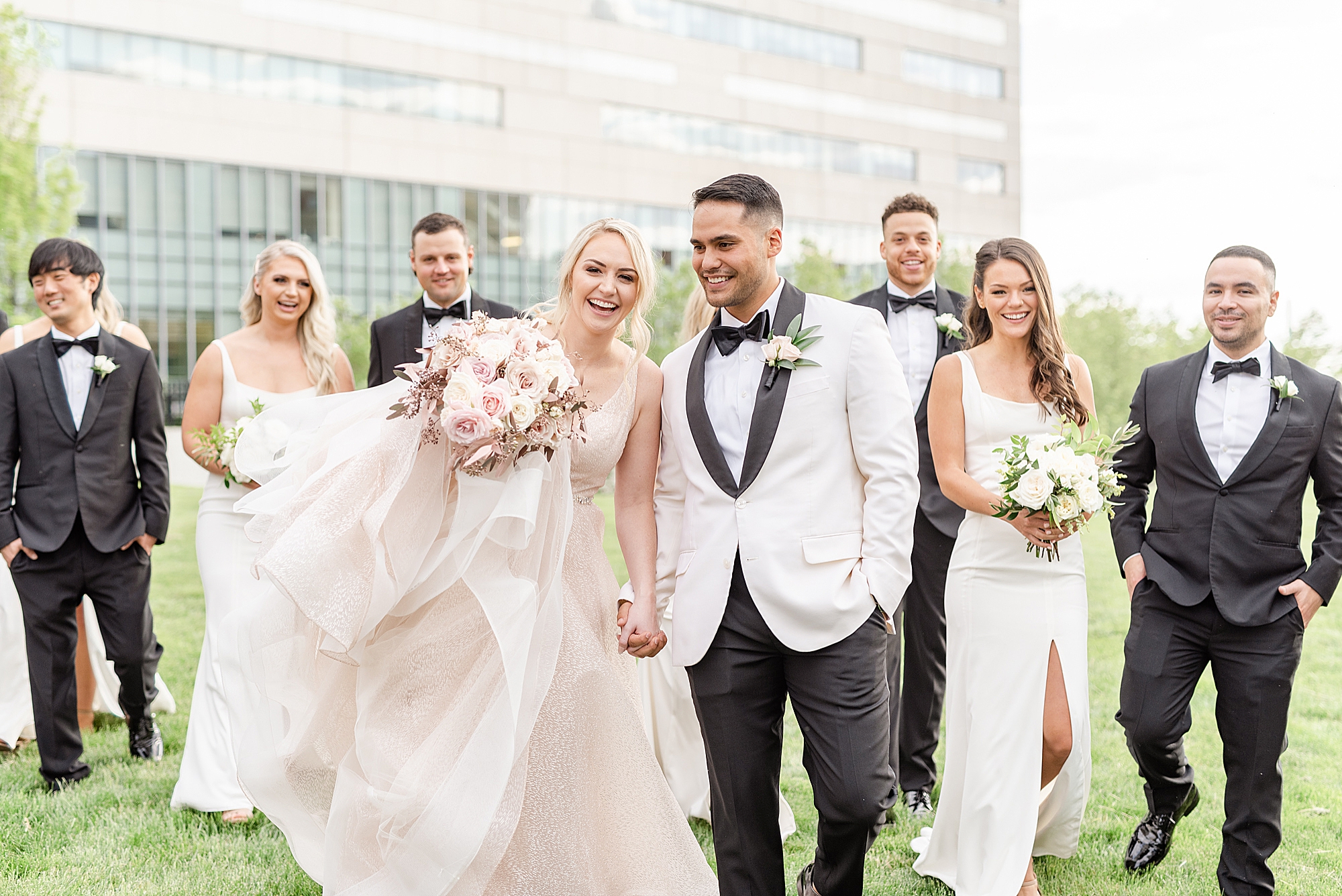 newlyweds hold hands walking with bridal party