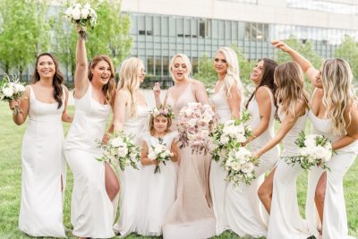 bridesmaids laugh with flower girl in all white dresses