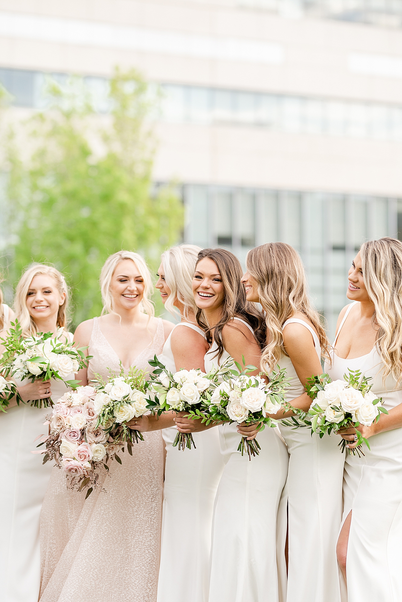 bridesmaids in white gowns smile with bride in blush wedding dress