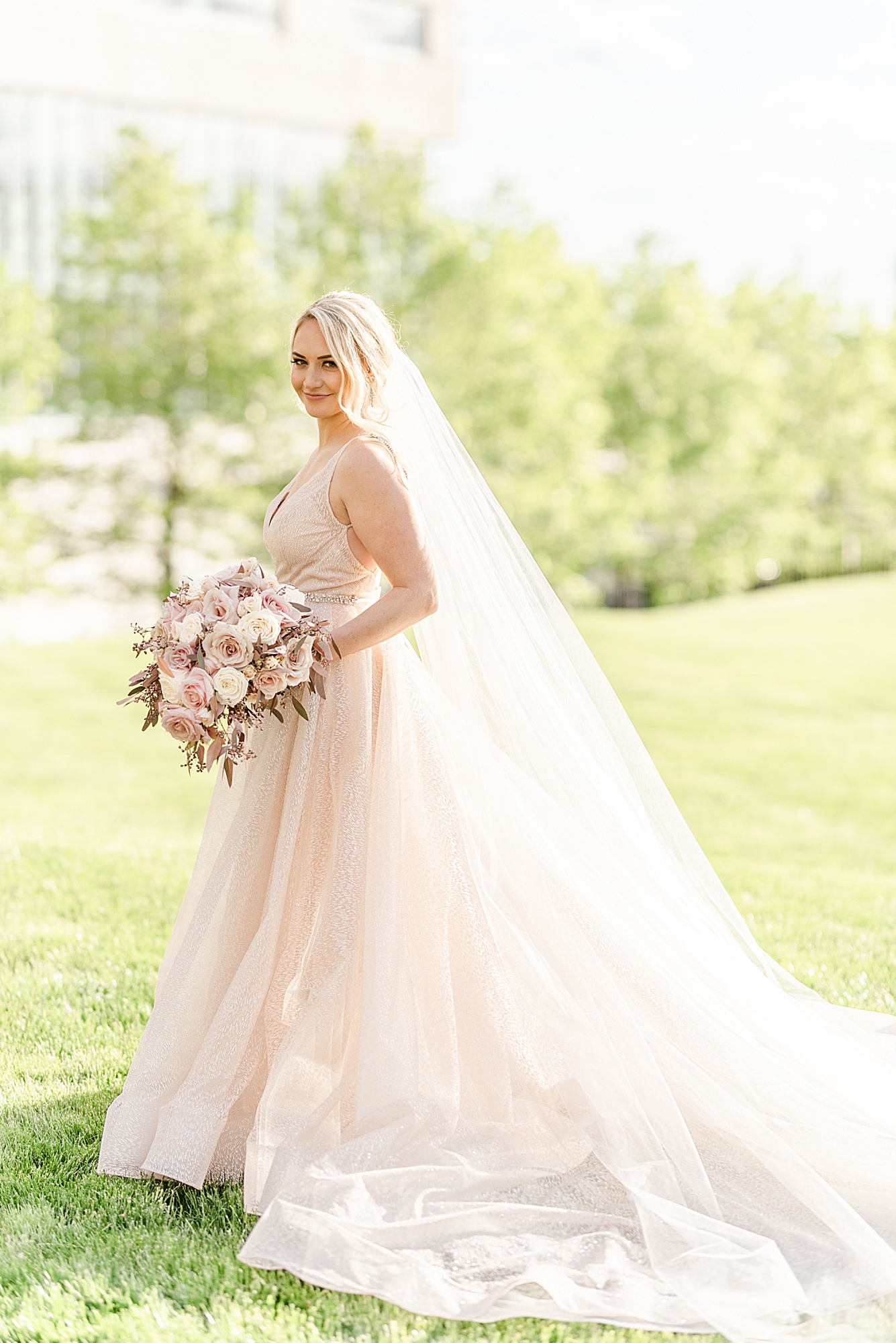 bride in blush pink gown holds bouquet by hip