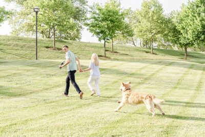 engaged couple walks with dog chasing them