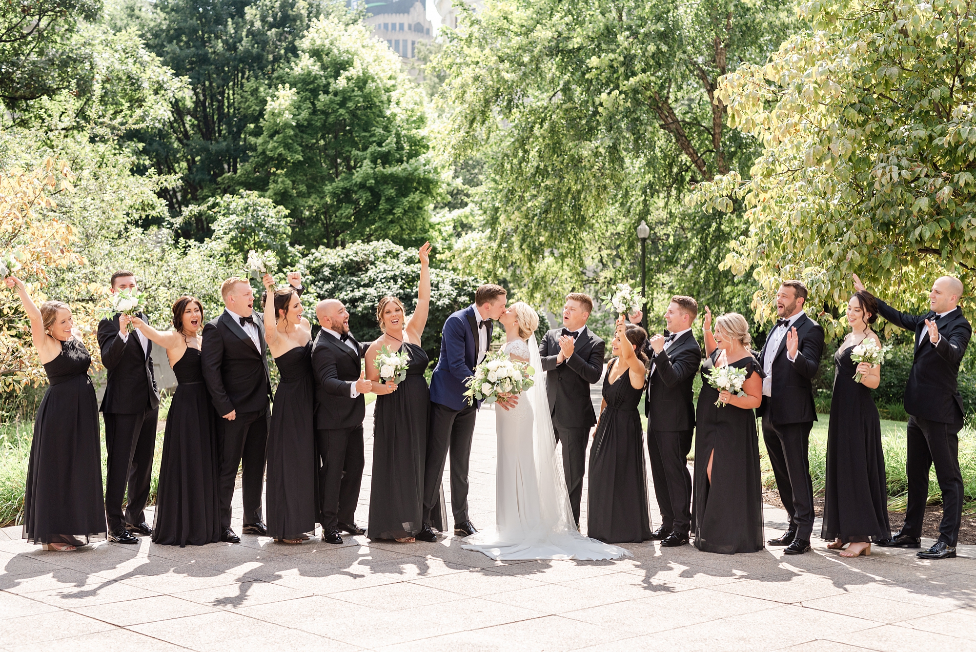 groom kisses bride with wedding party around them