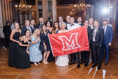 bride and groom pose with college alumni at wedding reception