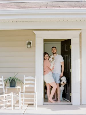 family poses on front porch with two dogs during fourth anniversary portraits