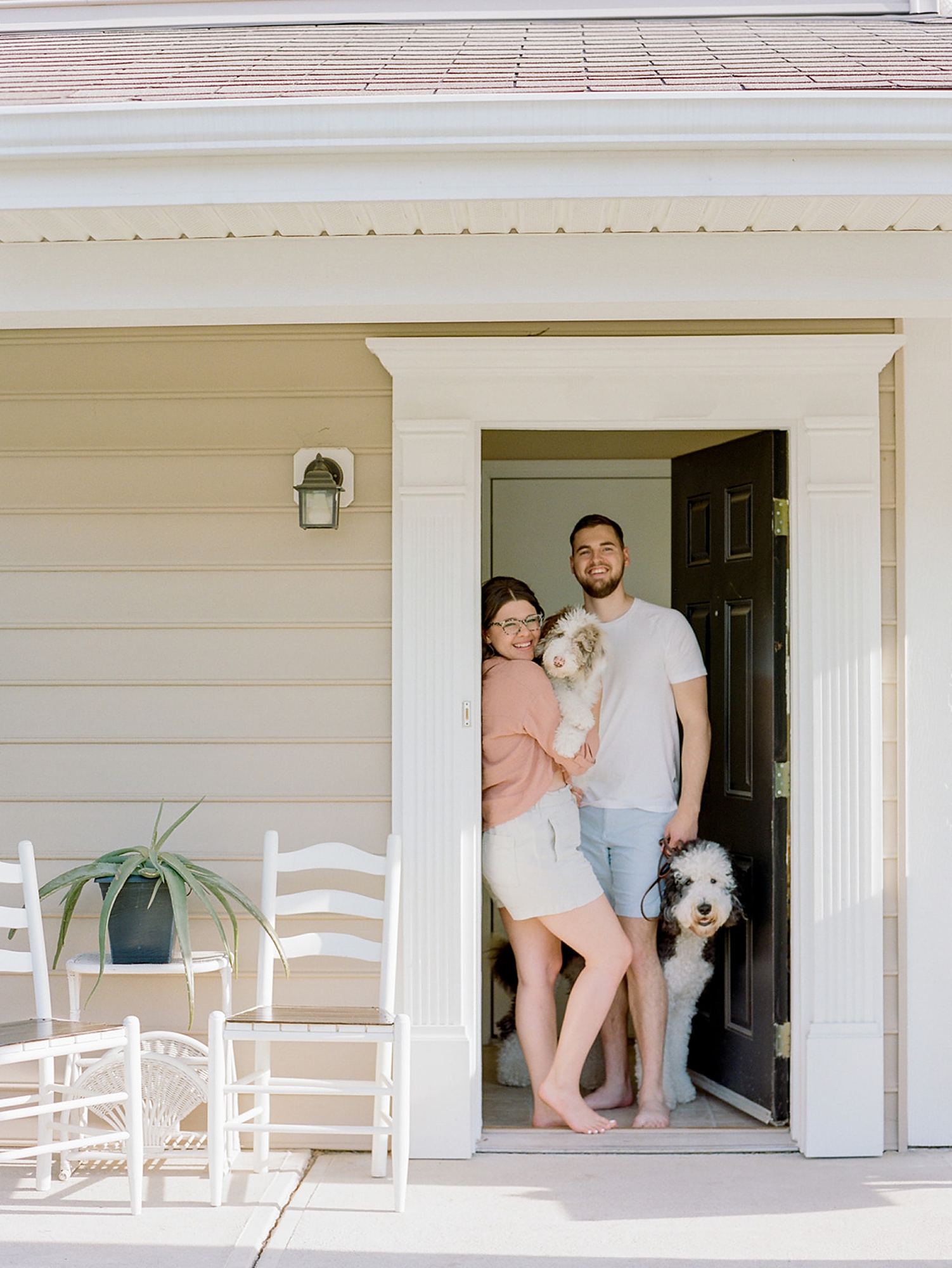 family poses on front porch with two dogs during fourth anniversary portraits