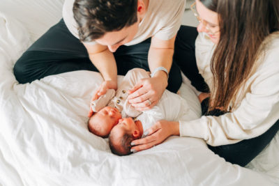new parents snuggle with babies on bed