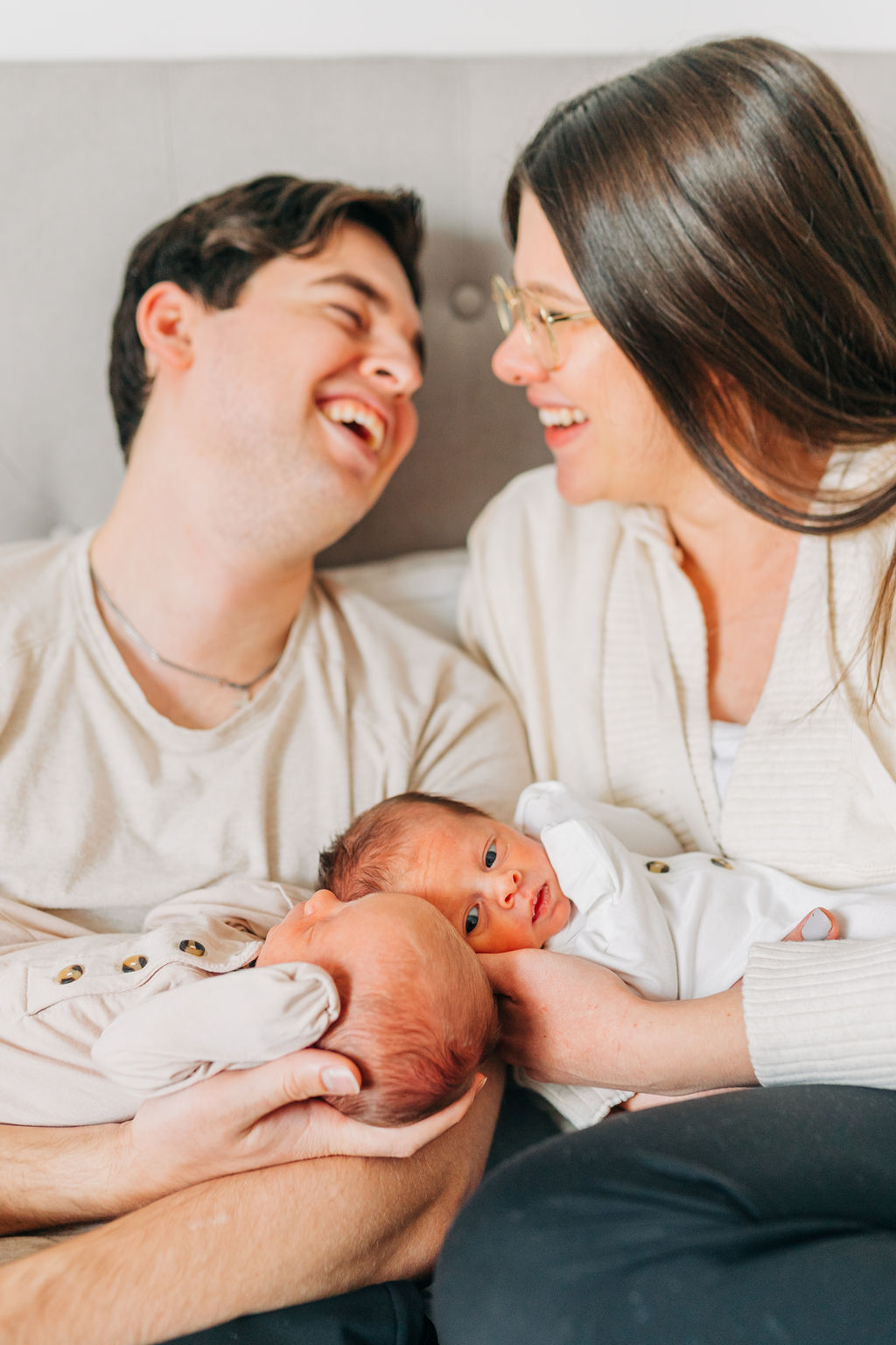 new parents laugh holding babies on bed